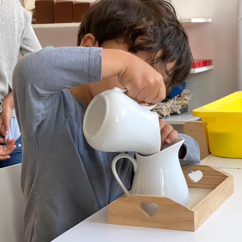 A child learns to pour a liquid with a carafe